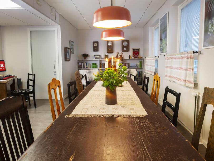 A dining area with a wooden table, chairs, a potted plant, and a hanging light fixture.