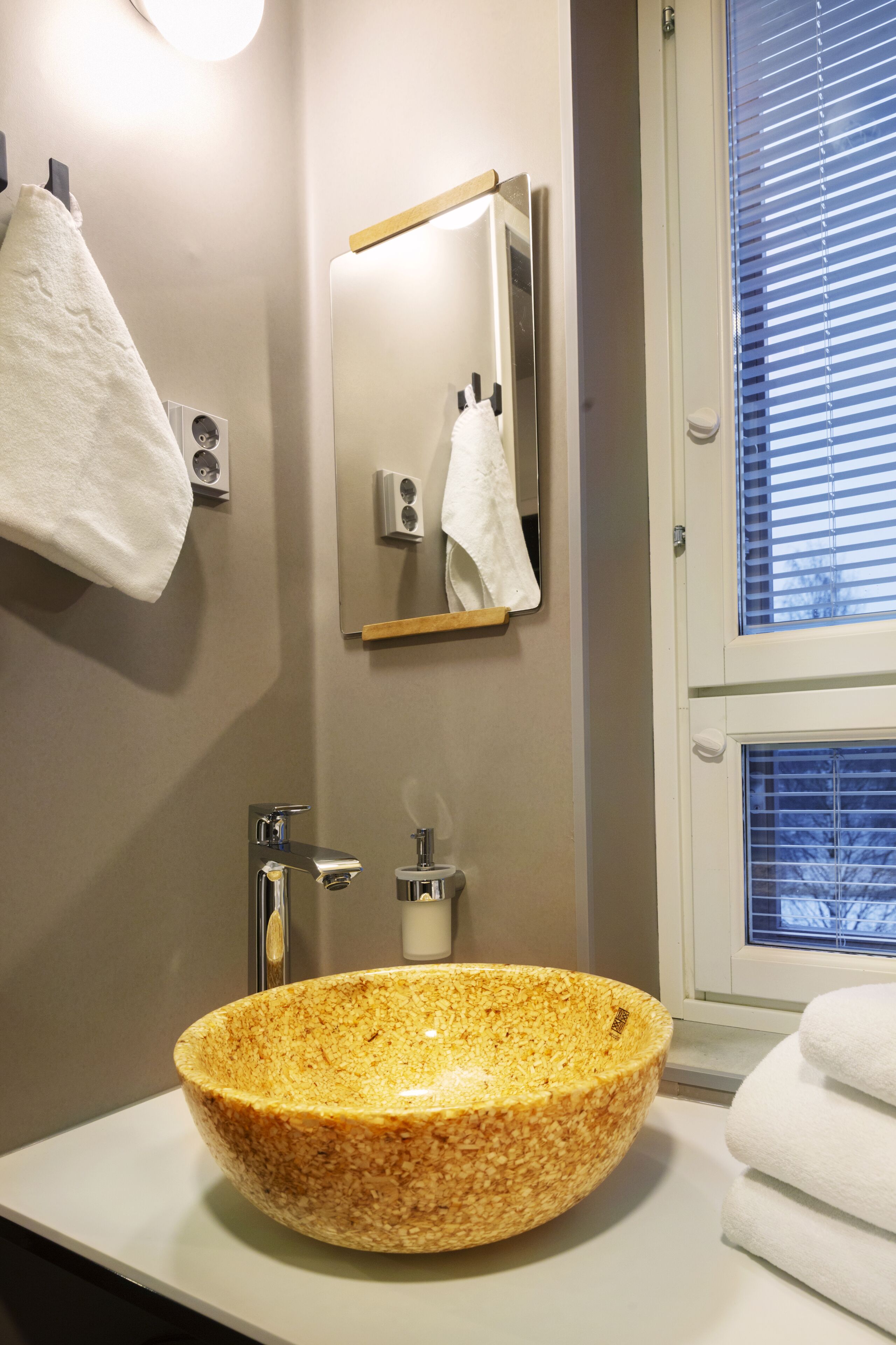 A bathroom with a large, textured bowl sink, a mirror, and a towel rack.