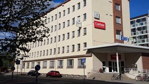 Un hotel de varios pisos con un llamativo letrero que dice 'Lietsu Boutique Apartment Hotel', una entrada para peatones y un estacionamiento con coches y bicicletas.