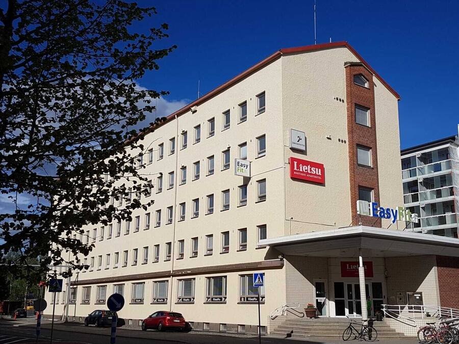 A multi-story hotel with a prominent 'Lietsu Boutique Apartment Hotel' sign, a pedestrian entrance, and a parking area with cars and bicycles.