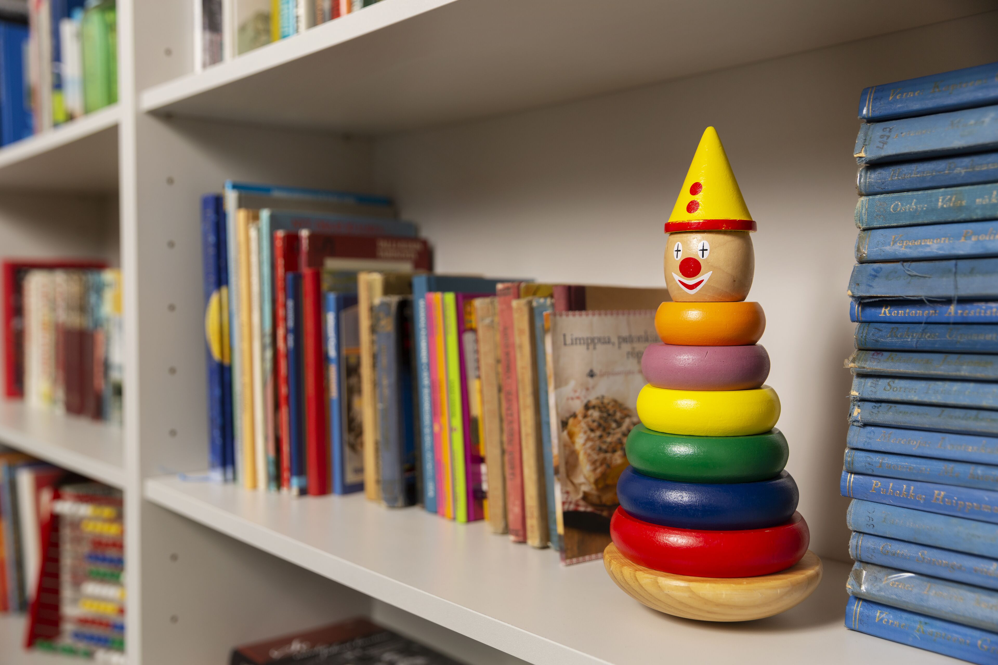 Ein Holzspielzeug mit Clownhut und Ringen auf einem Regal.