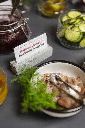 Une table avec un plat de hareng aux cassis, un pot de moutarde et un bol de concombres en tranches.