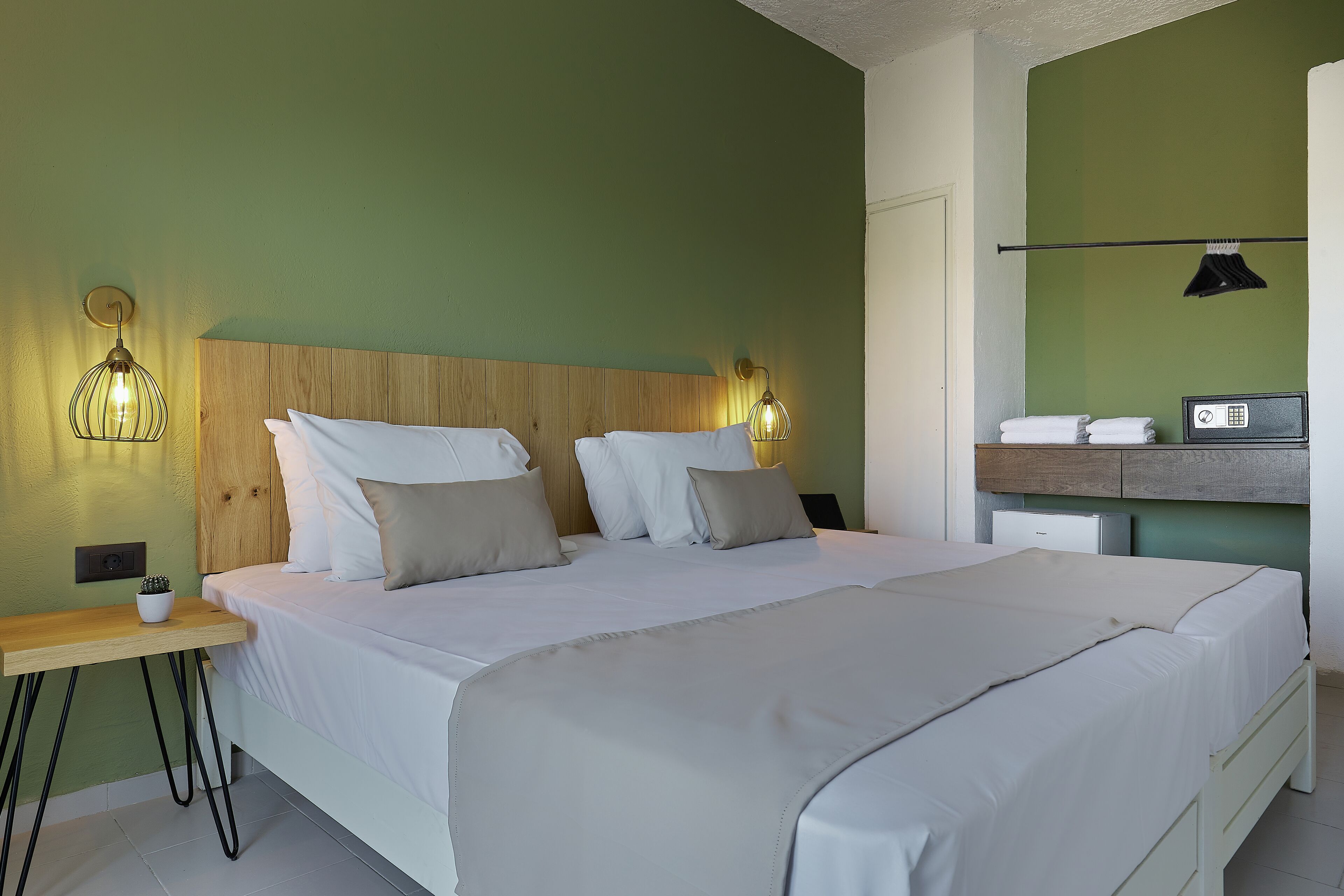 A neatly made double bed with a wooden headboard, two bedside tables with lamps, and a small bedside table with a plant.