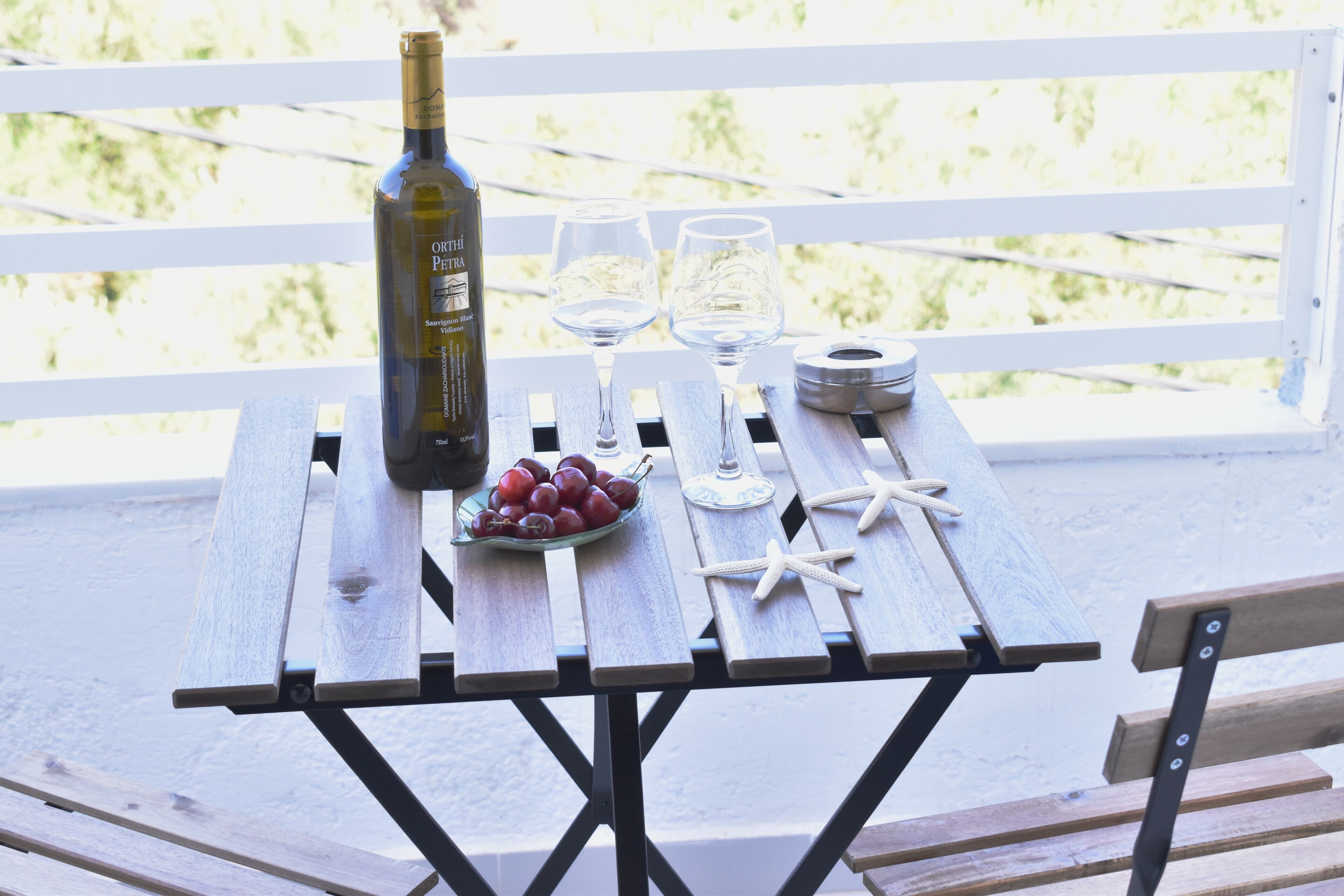 A wooden table with a bottle of wine, two glasses, a bowl of grapes, and starfish decorations.