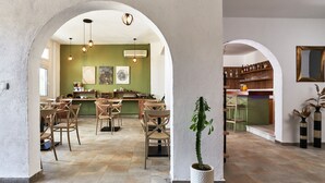 A spacious dining area with high ceilings and arched doorways, featuring a green wall with artwork, wooden chairs, and a potted plant. - Charm Hotel Hersonissos (Hersonissos)