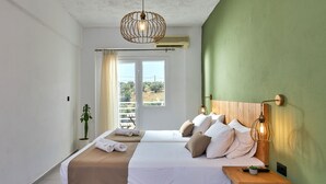 A bedroom with two beds, a wooden nightstand, a potted plant, and a view of the outdoors. - Charm Hotel Hersonissos (Hersonissos)