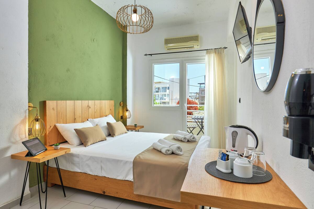 A hotel room with a bed, bedside table, lamp, and a view of the outside.