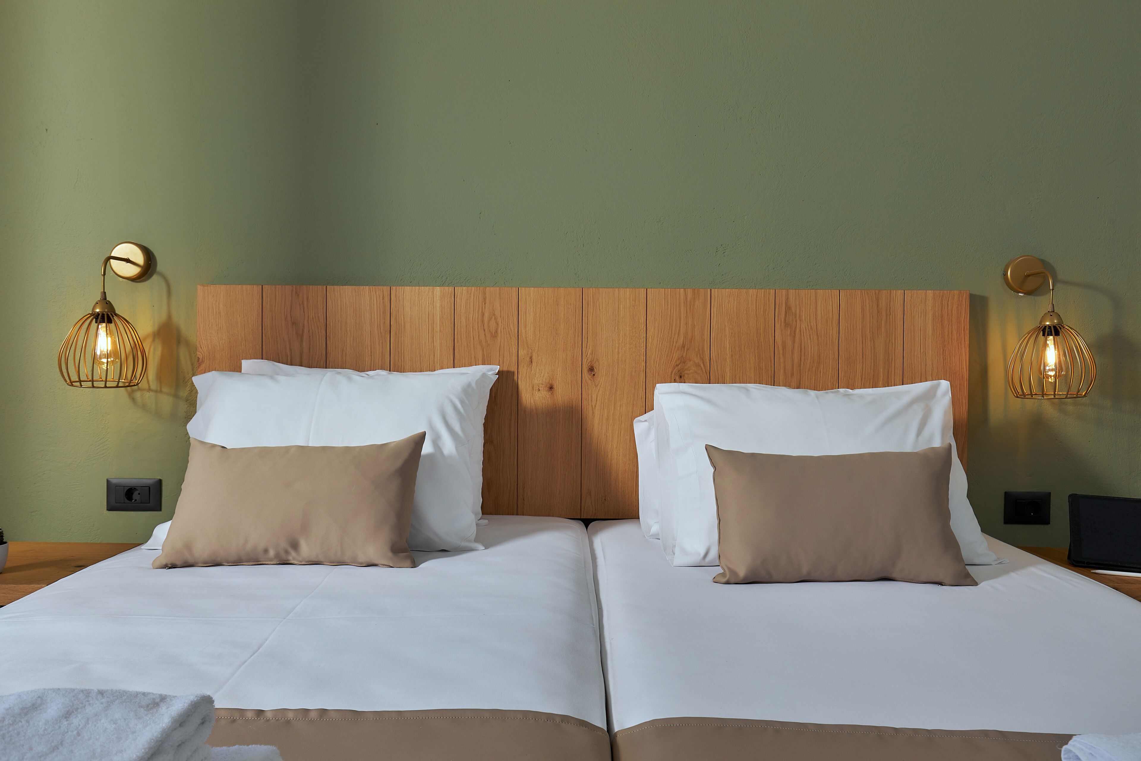 A double bed with white and beige bedding, two bedside tables, and two wall-mounted lamps.