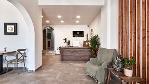 A hotel reception area with a wooden reception desk, a green armchair, a small table with a plant, and a framed picture on the wall. - Charm Hotel Hersonissos (Hersonissos)