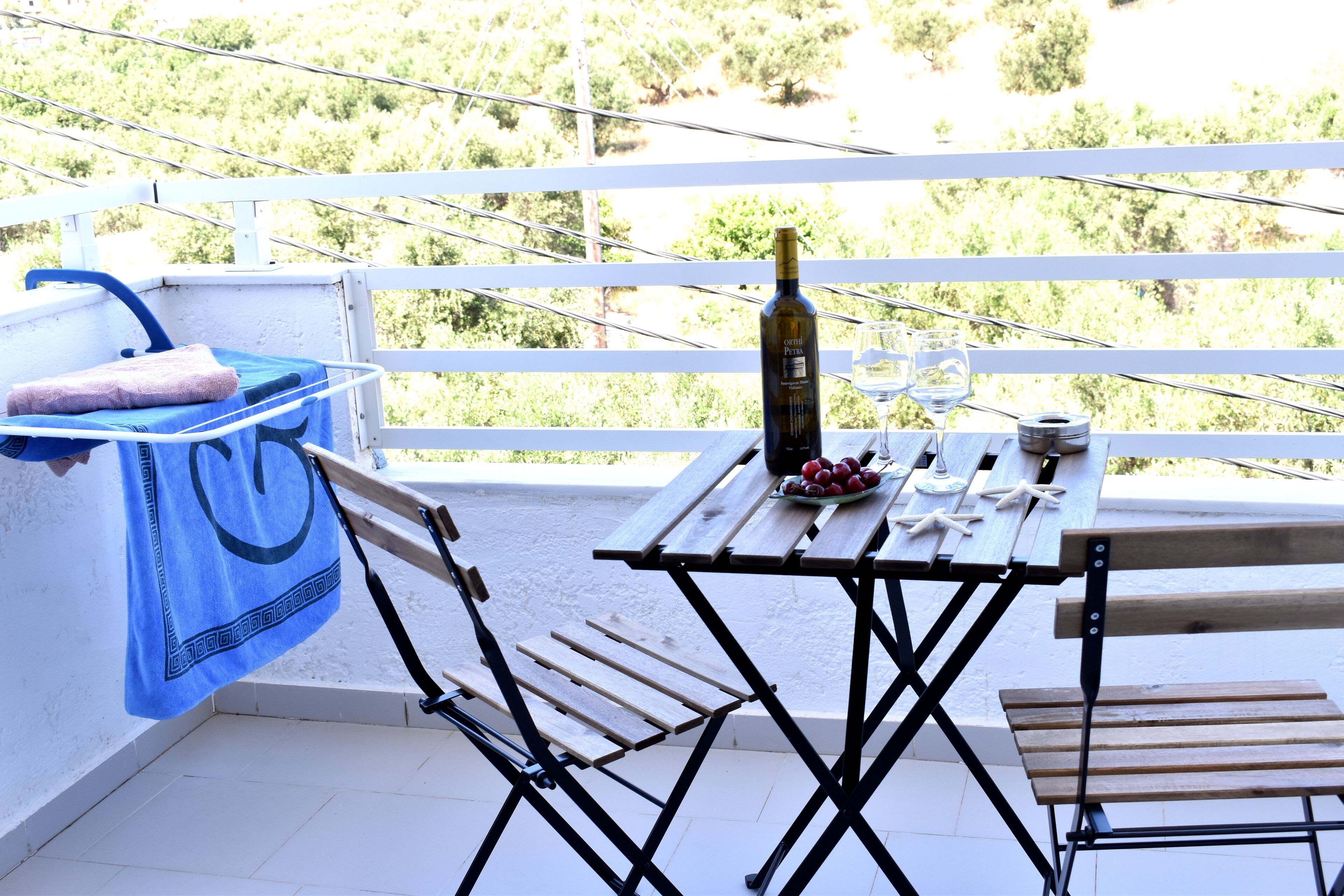 A balcony with a table set for two, a bottle of wine, and a bowl of fruit.
