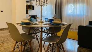 A dining area with a round table, four chairs, a candelabra, and a window with curtains.