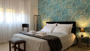 A neatly made bed with white linens and pillows, a bedside table with a lamp, and a chair.