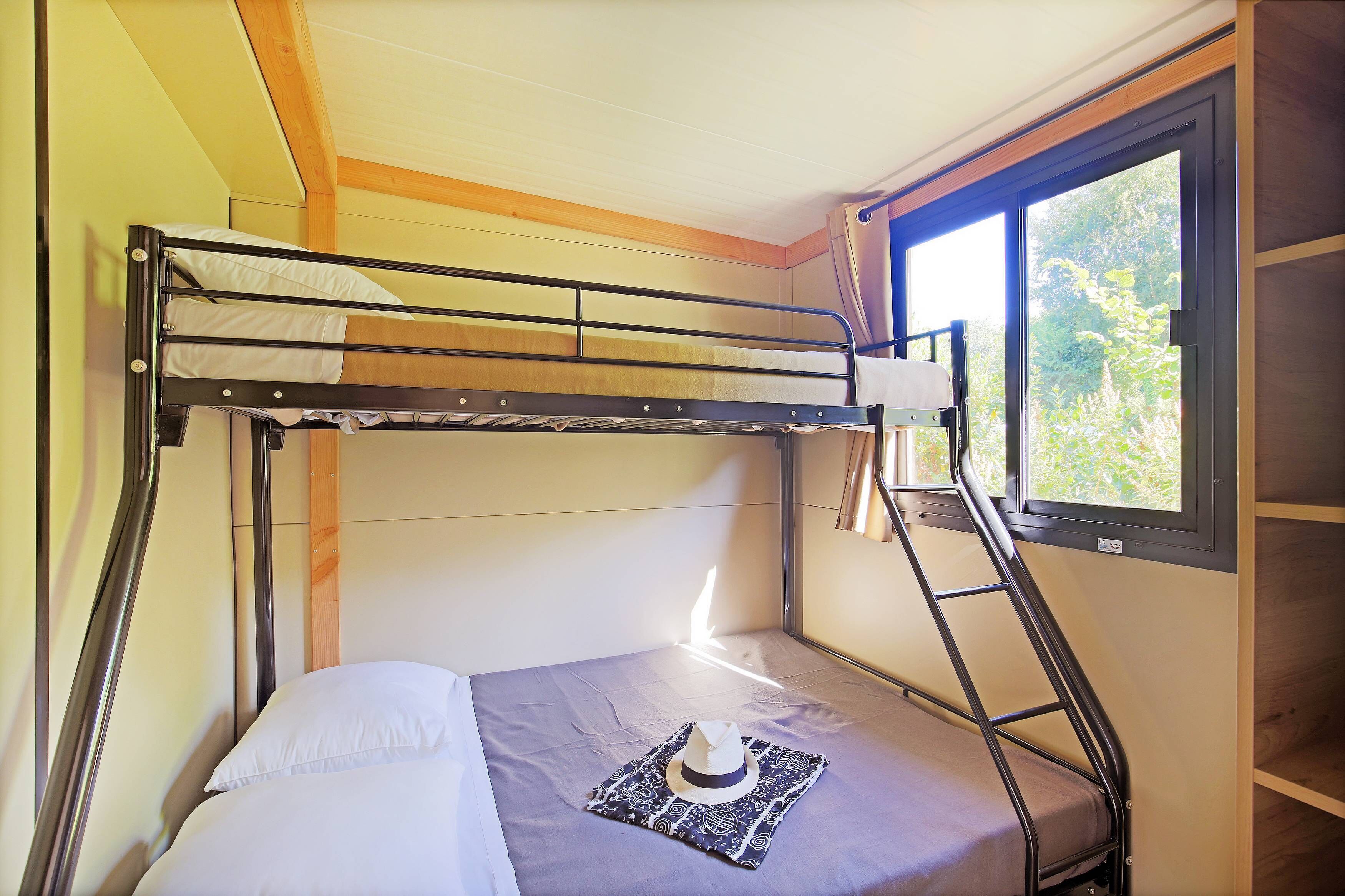 Una cama individual sobre otra con ventana, techo de madera y una pequeña mesa con un sombrero.