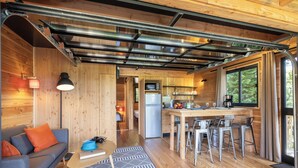 Una cocina moderna con detalles de madera, una zona de comedor con taburetes de bar y un sofá con cojines naranjas.