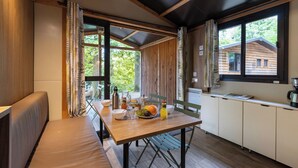 Acogedora habitación tipo cabaña con una mesa de madera dispuesta para el desayuno, un banco y vistas a otra cabaña a través de la ventana.