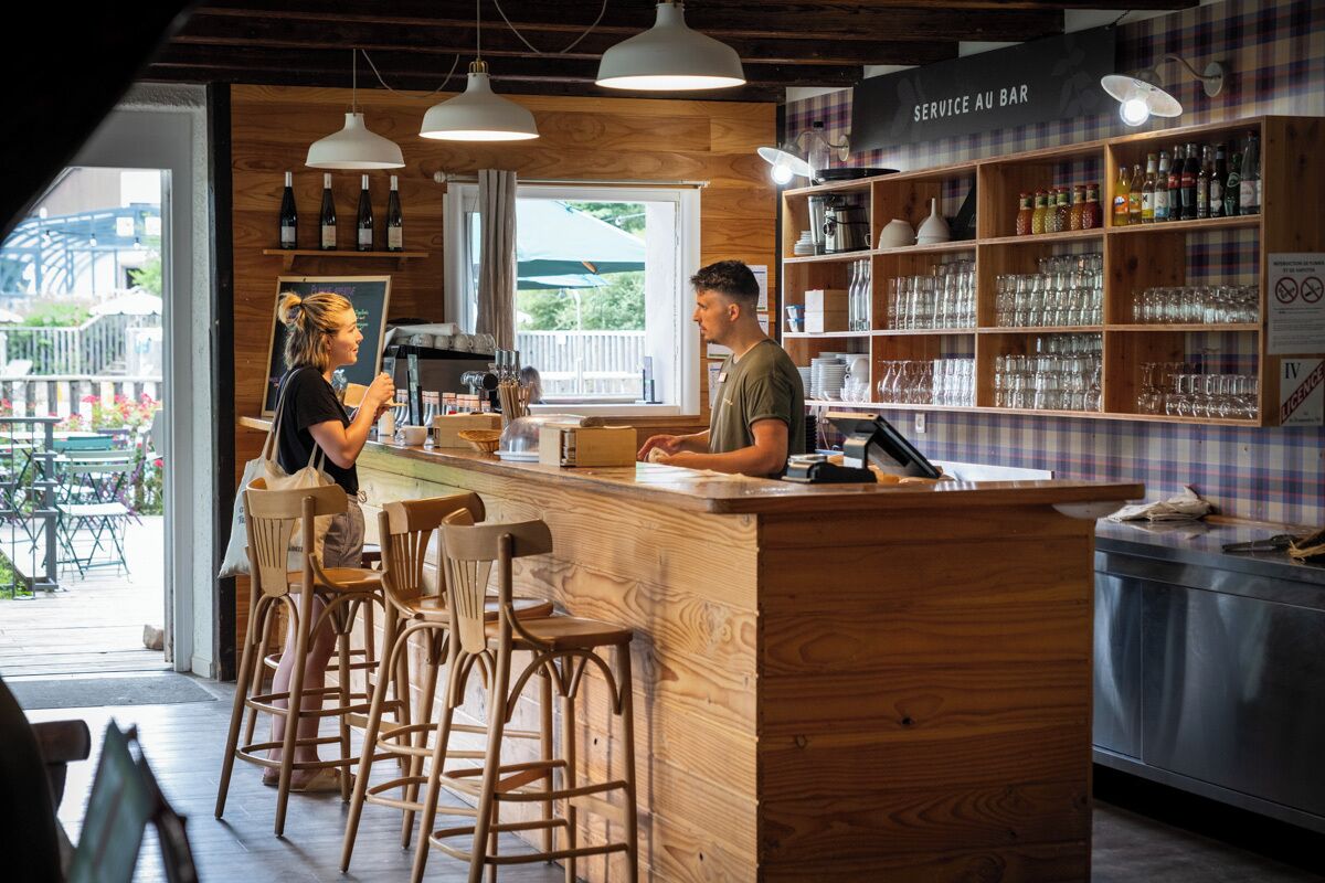 A bar area with wooden furniture, a bar counter, and shelves with bottles and glasses.