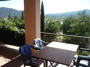 A balcony with a table and two chairs, overlooking a scenic landscape with hills and trees.
