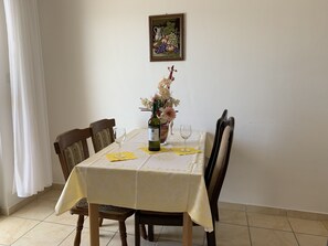 A dining table with a white tablecloth, two chairs, a bottle of wine, a glass, and a vase with flowers. - Apartment 1 with pool and amazing sea view (Lokva Rogoznica)