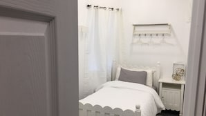 A small, white bedroom with a single bed, a nightstand, and a wall-mounted shelf. - Charm in the City (Baltimore)