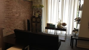 A living room with a brick wall, a black sofa, a small white table, and a wooden cabinet with decorative items. - Charm in the City (Baltimore)
