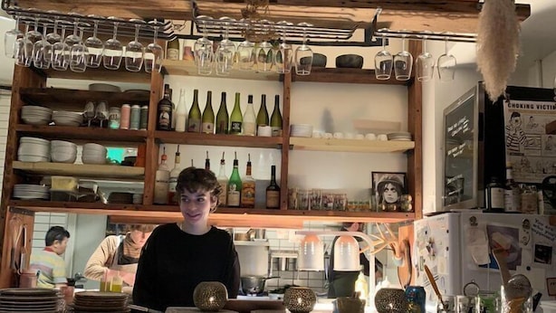 A bar area with shelves of bottles and glasses, a chalkboard menu, and a hanging light fixture. - Charm in the City (Baltimore)