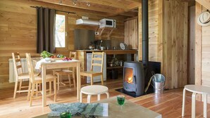A cozy cabin interior with a dining area, a kitchen with a stove, and a large window. - Village Huttopia Sud Ardèche (Vagnas)