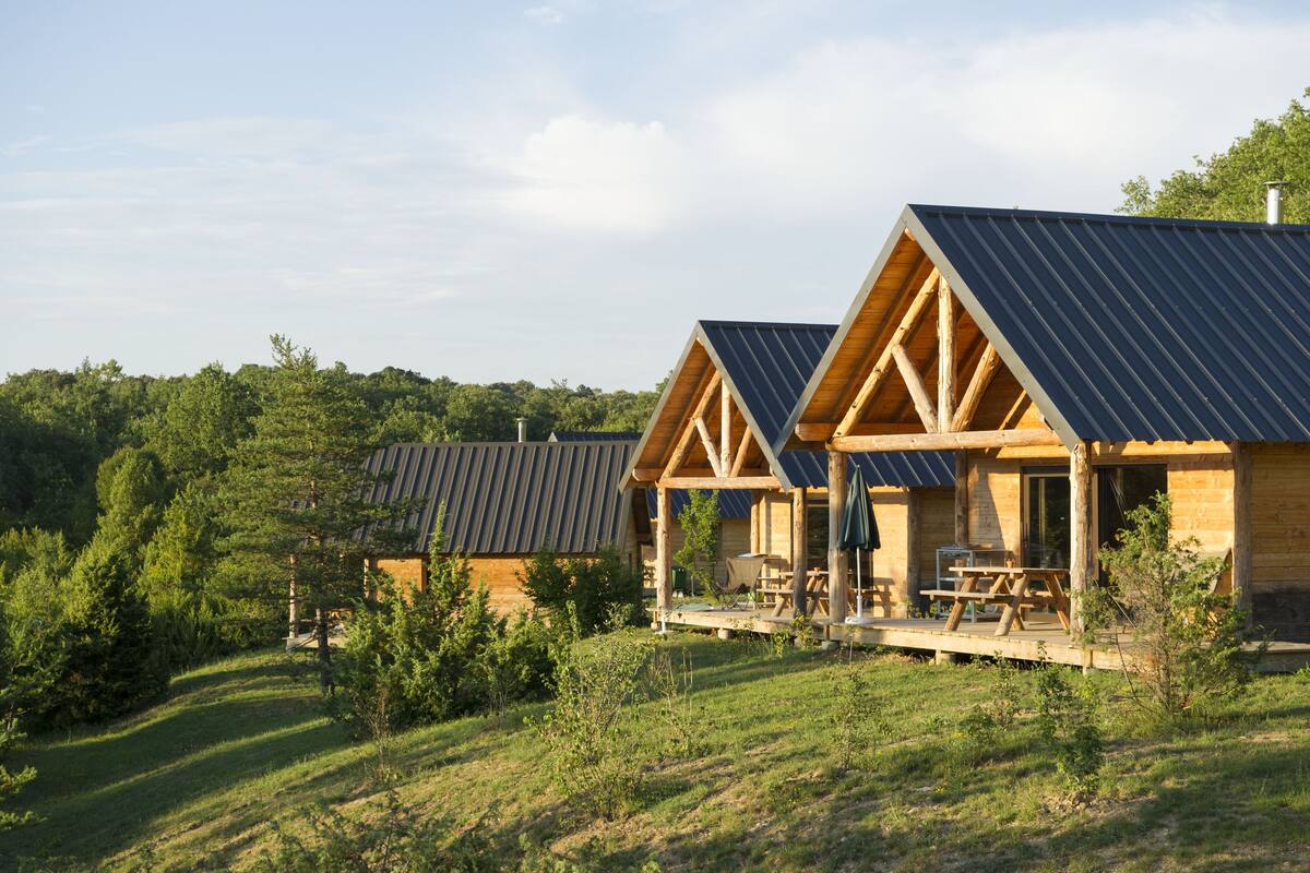 A cabin with a sloped roof, wooden exterior, and a covered porch with a table and chairs.