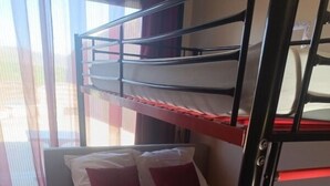A bunk bed with white bedding and red pillows, a window with curtains, and a tiled floor.