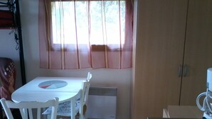 A small kitchen with a white table, two white chairs, a window with sheer curtains, and a coffee machine.