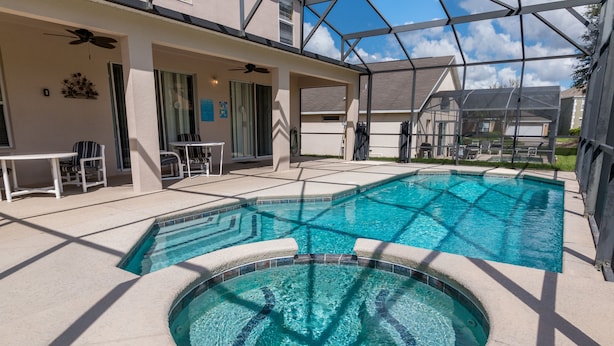 Una piscina con hidromasaje, mobiliario exterior y un patio cubierto.