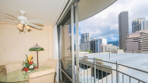 A balcony with a glass table, a chair, a ceiling fan, and a view of tall buildings. - Charming Ilikai Marina Studio, Great Location In Waikiki! (Honolulu)