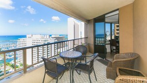 Uma varanda com mesa e cadeiras, com vista para uma marina e edifícios, e uma visão clara do oceano.