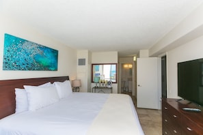 A hotel room with a large bed, a TV, a desk with a lamp, and a painting on the wall.