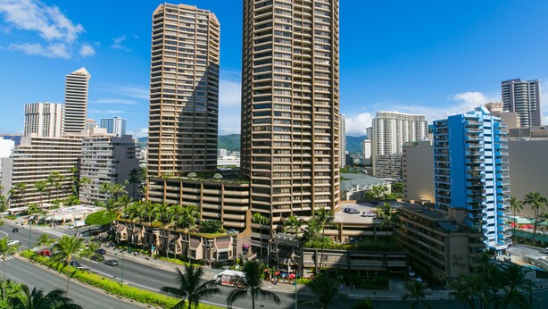 Paisagem urbana com edifícios altos e modernos, incluindo um hotel de destaque com fachada azul e bege.