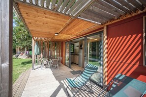 Un espace extérieur abrité doté d’une terrasse en bois, d’une porte vitrée donnant sur l’intérieur et d’un mur rouge.