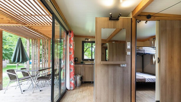Un espacio habitable moderno y compacto con interior de madera, una pequeña cocina y un patio con mobiliario exterior.