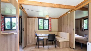 Habitación compacta con suelo de madera, una mesa con sillas, un banco y una cama.