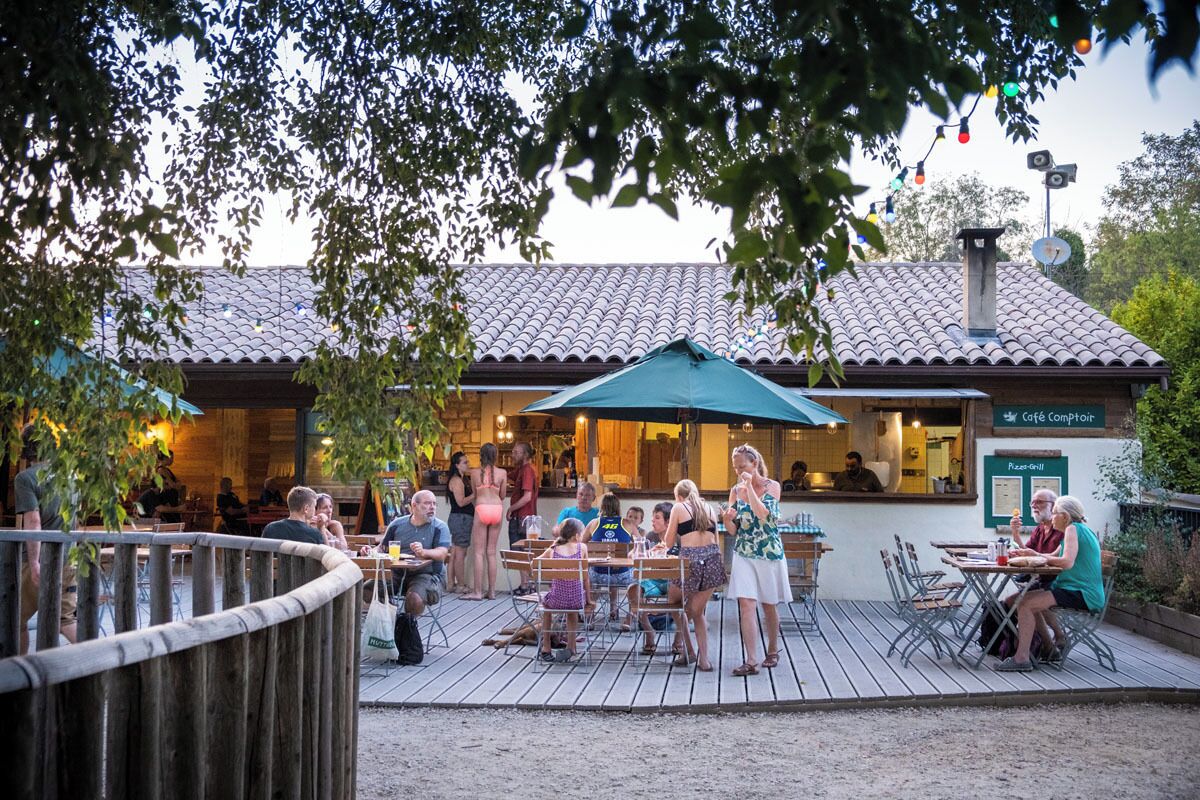 Een terras met tafels en stoelen, een houten dek en een gebouw met een betegeld dak op de achtergrond.