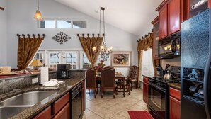 A kitchen with granite countertops, wooden cabinets, a stainless steel sink, a dining area with a table and chairs, and a red rug.