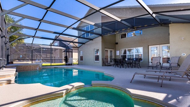 A swimming pool with a glass ceiling, surrounded by lounge chairs and a patio area.