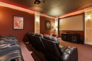 Sala de cine en casa con asientos reclinables de cuero, una pantalla grande y un sistema de sonido.