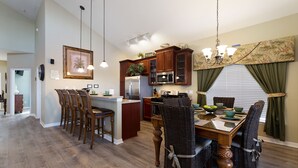 A spacious kitchen with wooden cabinets, a central island, and a dining area with wicker chairs.