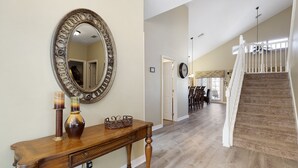 A spacious hallway with a wooden console table, a large mirror, and a staircase leading to an upper level.