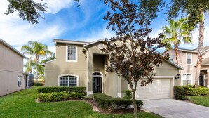 A two-story house with a front garage, a well-maintained lawn, and a mature tree in the front yard.