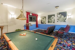 Et billardbord med bolde, en poolstang og en rød gardin. Fire stole og et bord med en vase.