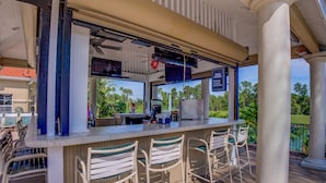 An outdoor bar area with a counter, bar stools, and a view of the surrounding greenery. - Emerald Blossom by VillaDirect (Kissimmee)