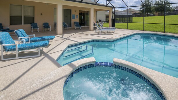 A swimming pool with lounge chairs and a hot tub, surrounded by a covered patio area. - Emerald Blossom by VillaDirect (Kissimmee)
