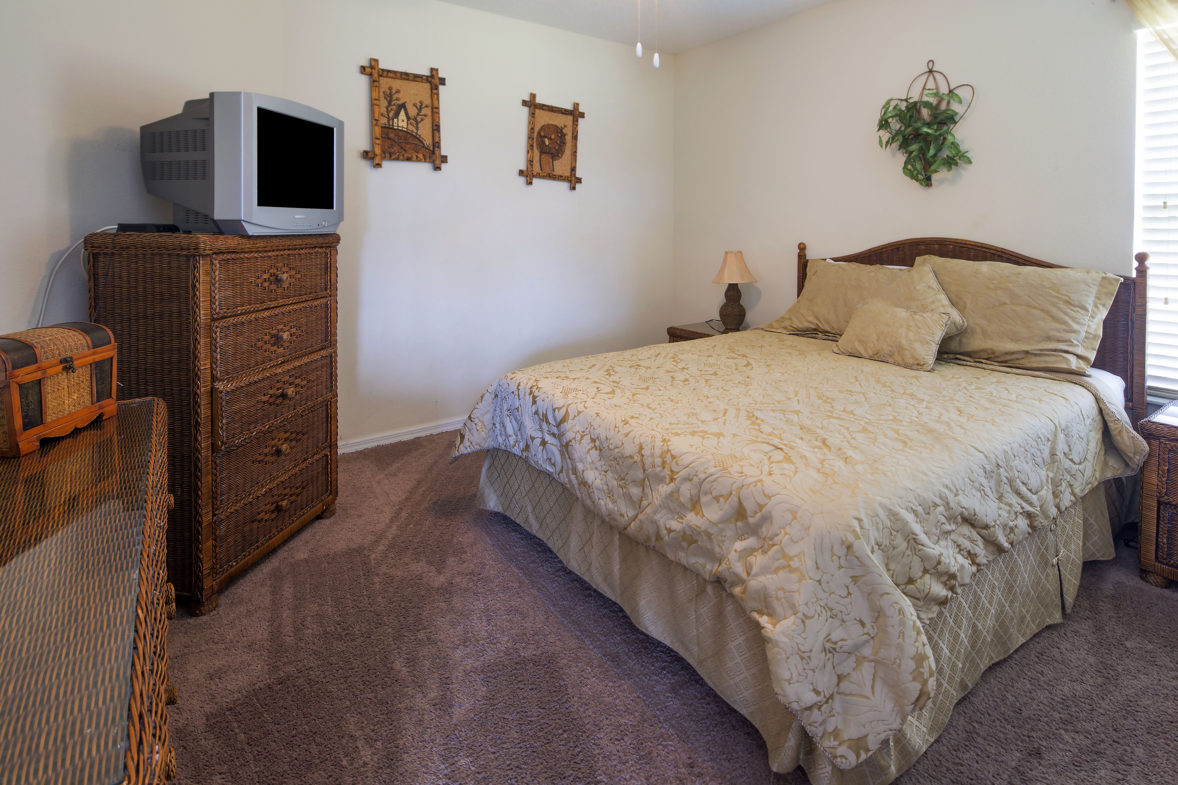 A bedroom with a bed, a dresser, a television, and two wall-mounted pictures.