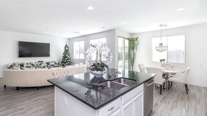 A modern kitchen with a central island, white cabinetry, and a dining area with a glass table and white chairs. - BUTTERFLY Lounge w/2 Masters - 12 min f/the Strip (Las Vegas)