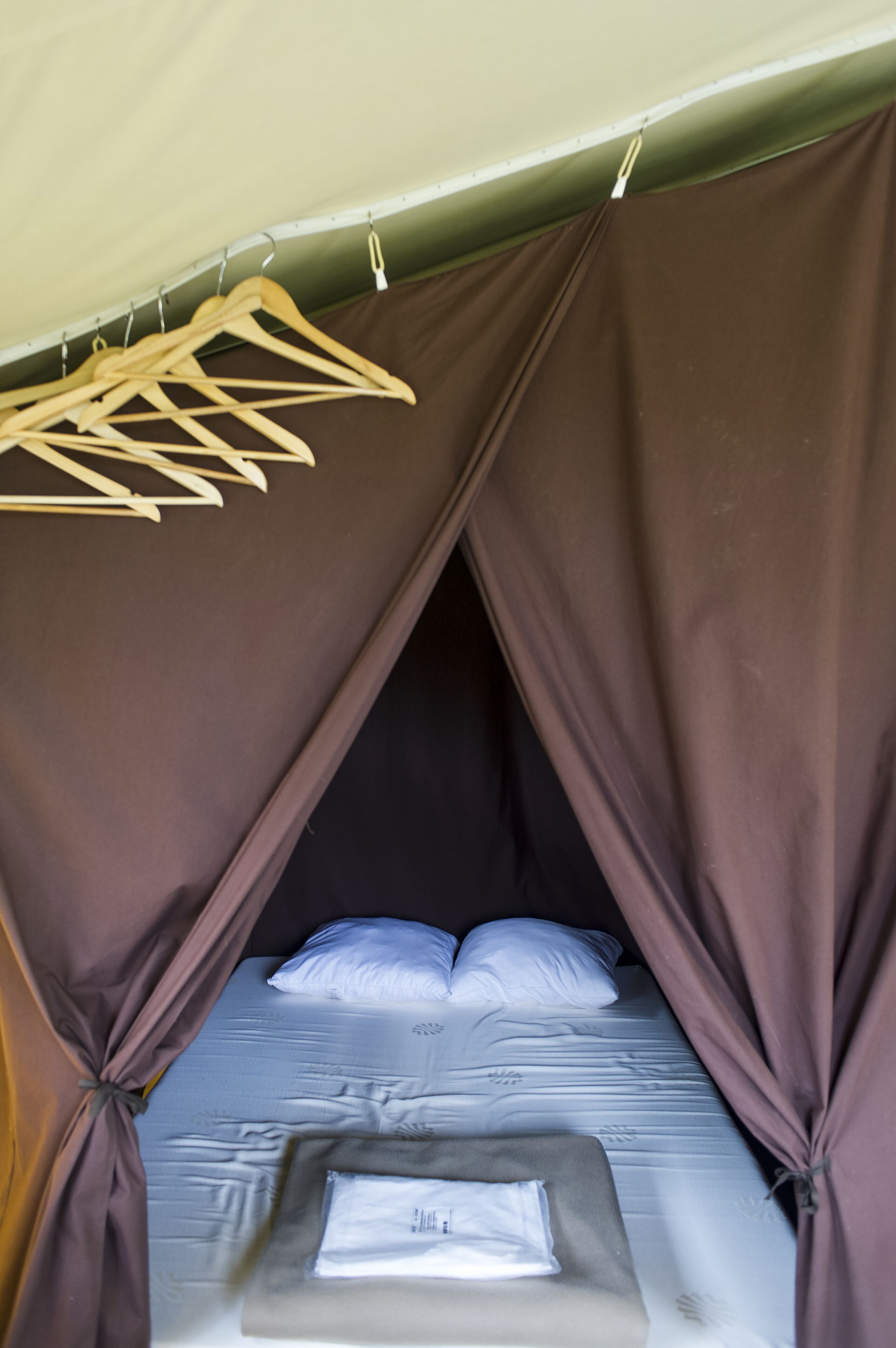 Une pièce aménagée comme une tente, avec un lit, un portant à vêtements et des rideaux.